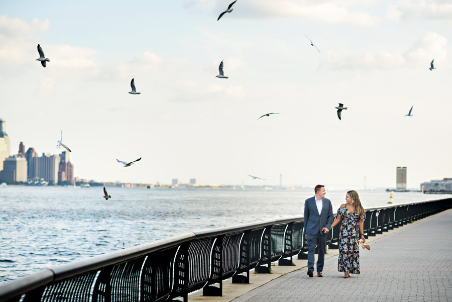 A beautiful couple walk along the hudson in Hoboken, NJ with birds flying all around them.